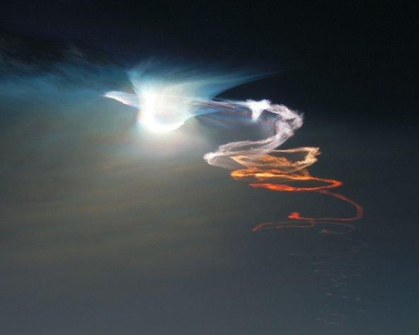 Этот великолепный вид плывущего по вечернему небу и закручивающегося следа ракеты, освещенного ярким светом заходящего Солнца и бледным сиянием восходящей Луны, можно было увидеть около Райтвуда в Калифорнии, США 19 сентября, за четыре дня до осеннего равноденствия. Цифровое изображение было получено с помощью телеобъектива, направленного на запад, в Обсерватории Столовая гора. Во время экспозиции твердотопливная ракета Минутмен III была уже далеко за пределами поля зрения. Запущенная с базы ВВС США Ванденберг, она несла пробный груз на тысячи миль над Тихим океаном. Красно-оранжевый свет заходящего Солнца окрашивает верхнюю часть следа ракеты в еще более насыщенные цвета. Нижняя часть следа, под линией заката, слабо освещена с востока почти полной Луной. В верхней части следа видно все еще освещенное Солнцем яркое размытое облако - результат разделения ступеней ракеты. Его края окрашены во все цвета радуги из-за преломления света в кристаллах льда, образовавшихся на большой высоте в струе выброшенного ракетой газа. Астроном Джеймс Янг заметил, что облако похоже на белого голубя, летящего по небу справа налево.
